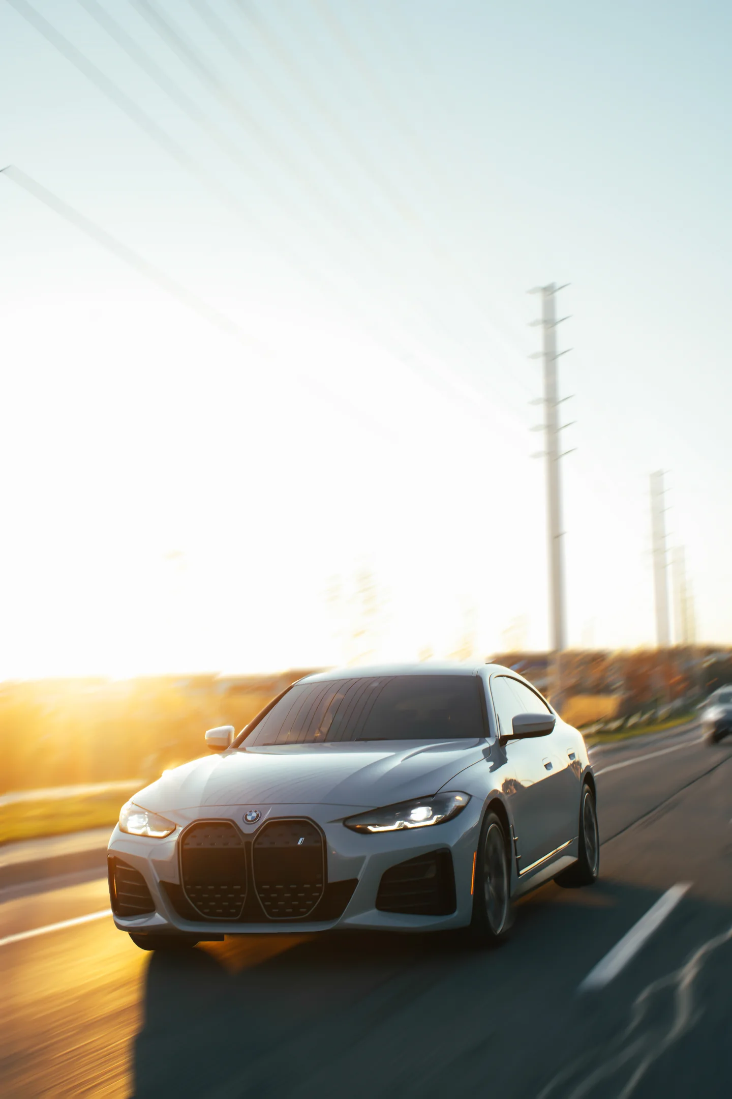 A BMW i4 in a rolling shot, background pulled into blur, low sun flaring off the bodywork.