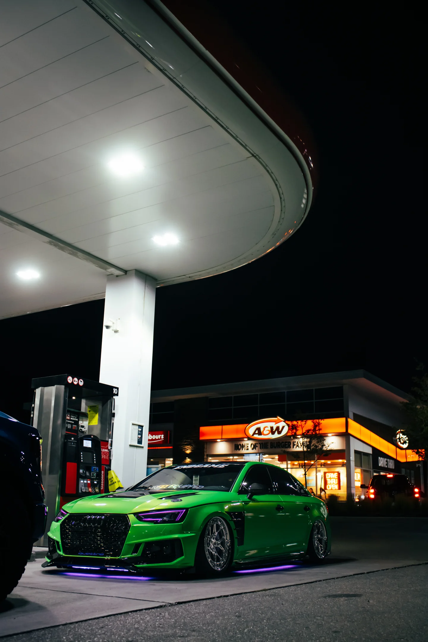 A green Audi S4 head-on beneath a gas station canopy with lit signage burning behind it.