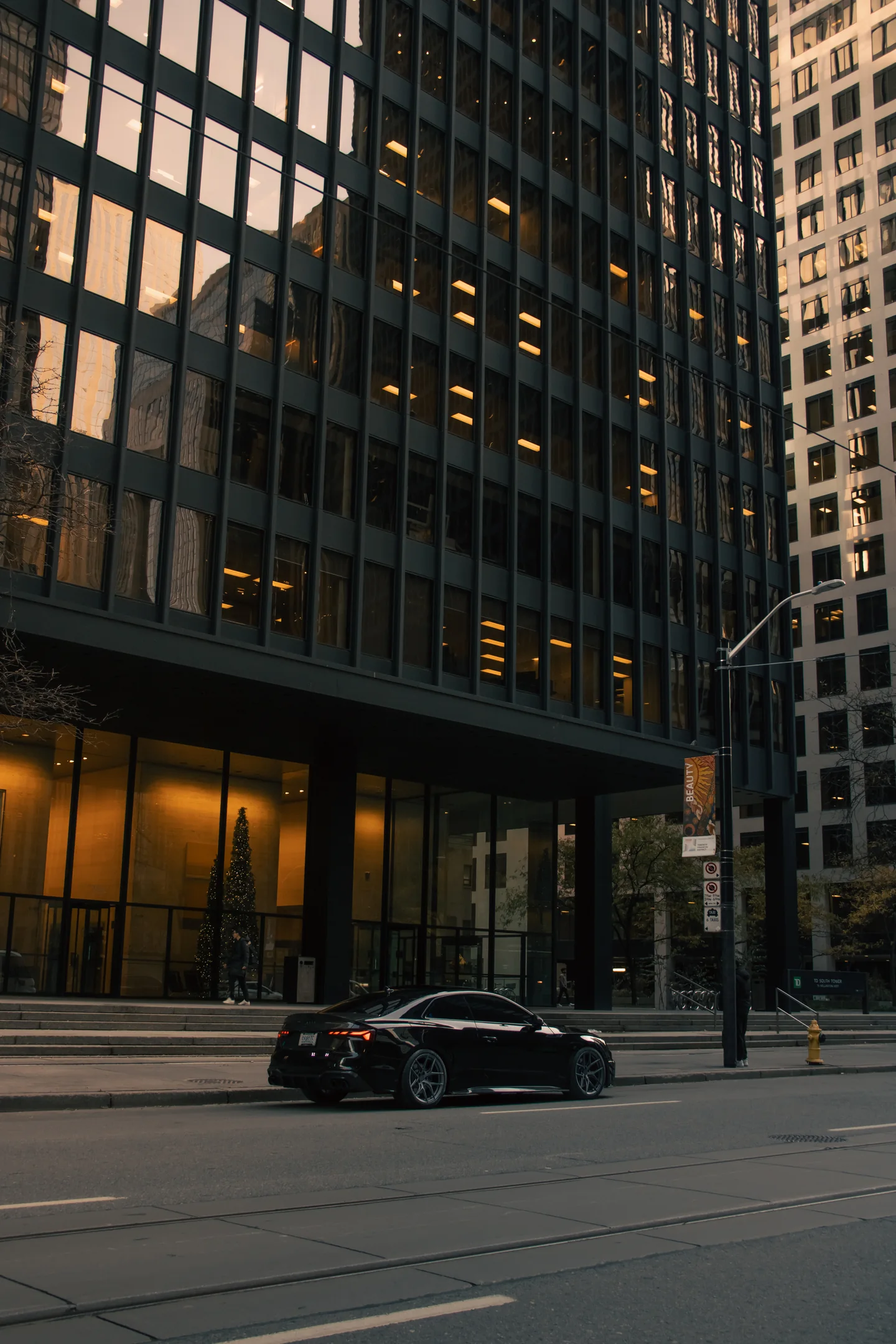 A black Audi S5 made small by the glass office towers of downtown Toronto at last light.