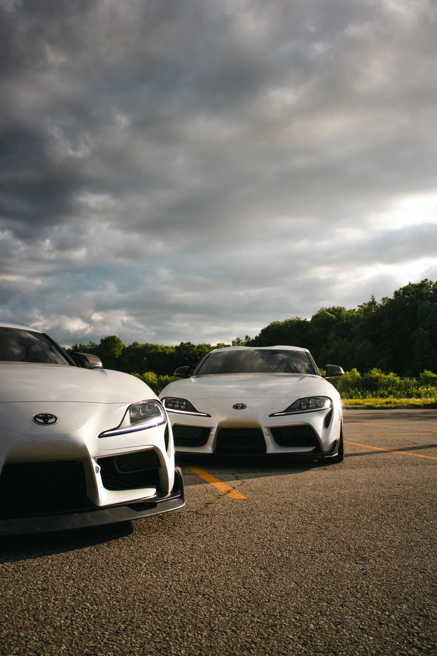 Two white Toyota Supras side by side as the cloud cover goes heavy overhead.